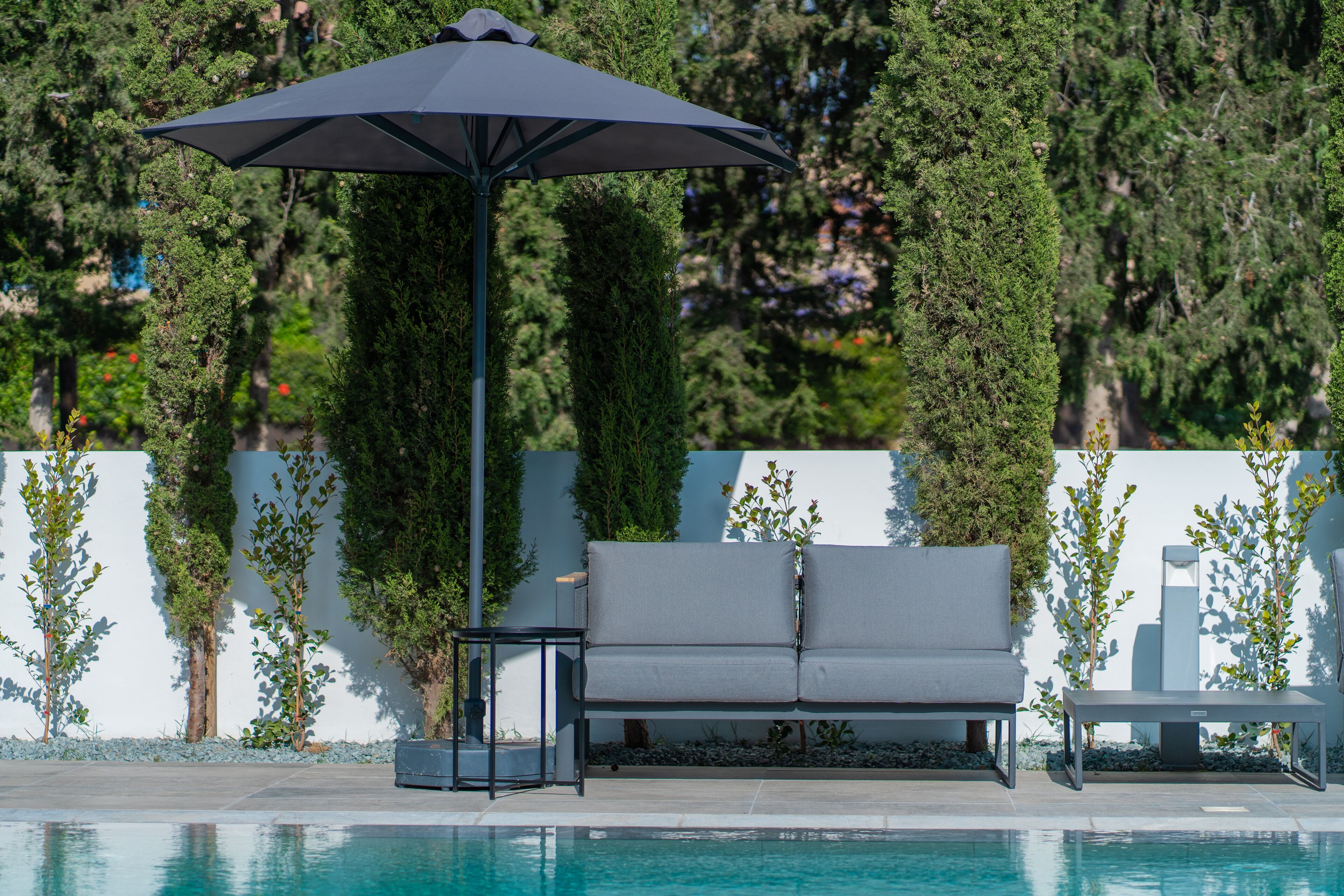 A poolside area with a grey sofa, a small table, and a large umbrella.