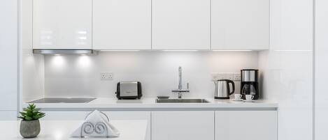 A modern kitchen with white cabinetry, a stainless steel range hood, a toaster, a coffee maker, and a sink.