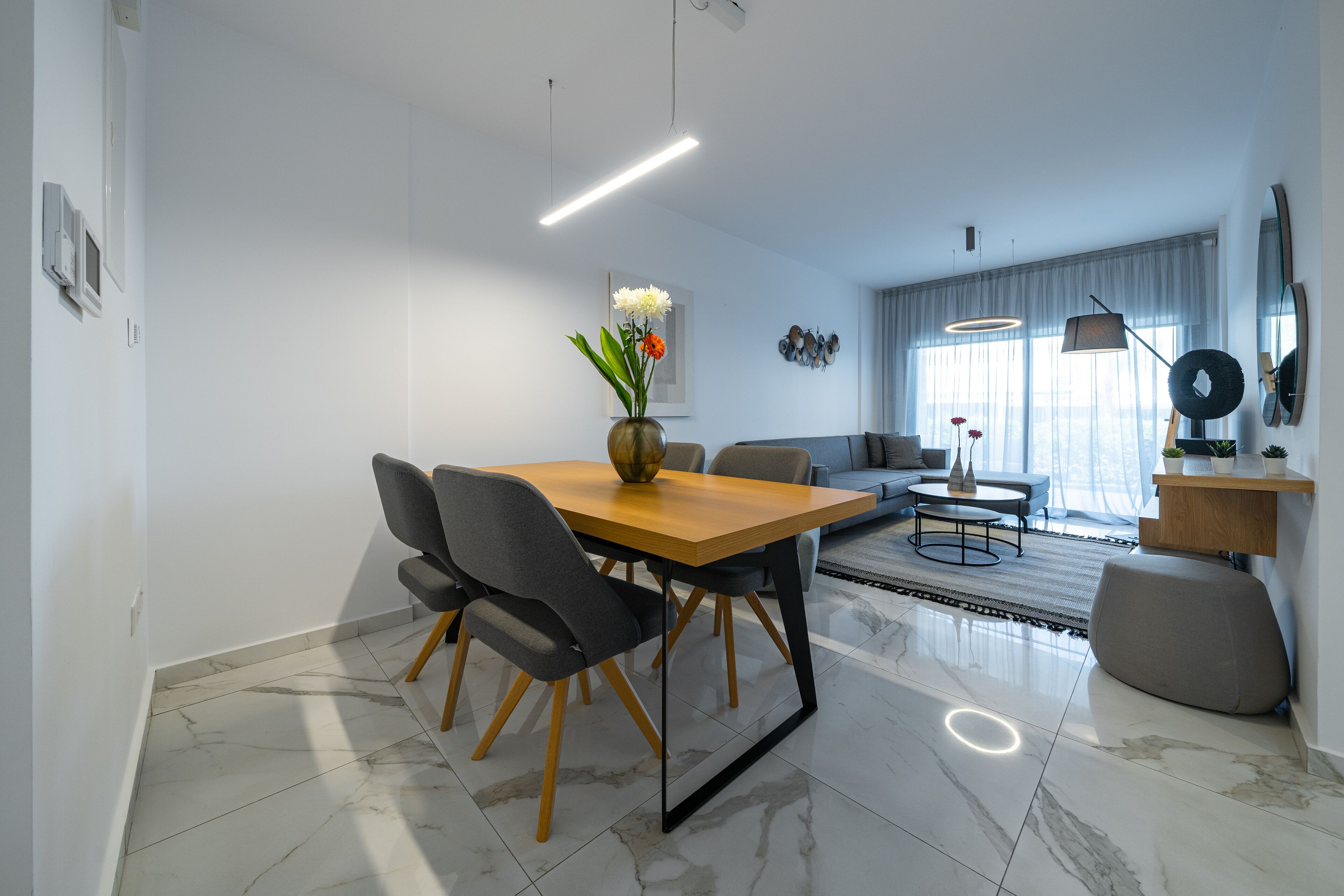 Un soggiorno moderno con zona pranzo, caratterizzato da un pavimento in marmo, un tavolo da pranzo in legno con sedie, un divano e un tavolino.