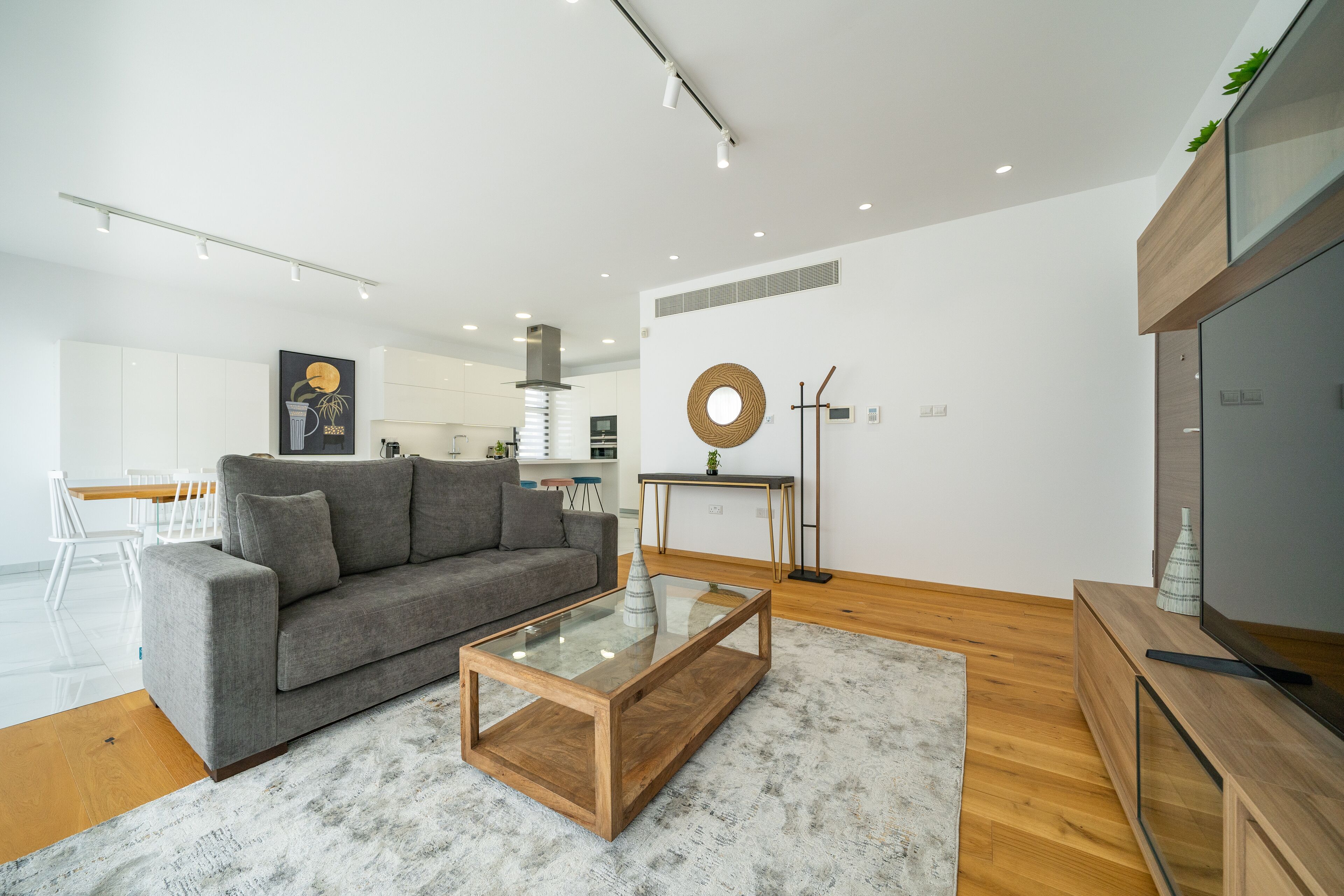 A modern living room with a grey sofa, a glass coffee table, and a wooden TV stand.