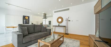 A modern living room with a grey sofa, a glass coffee table, and a wooden TV stand.