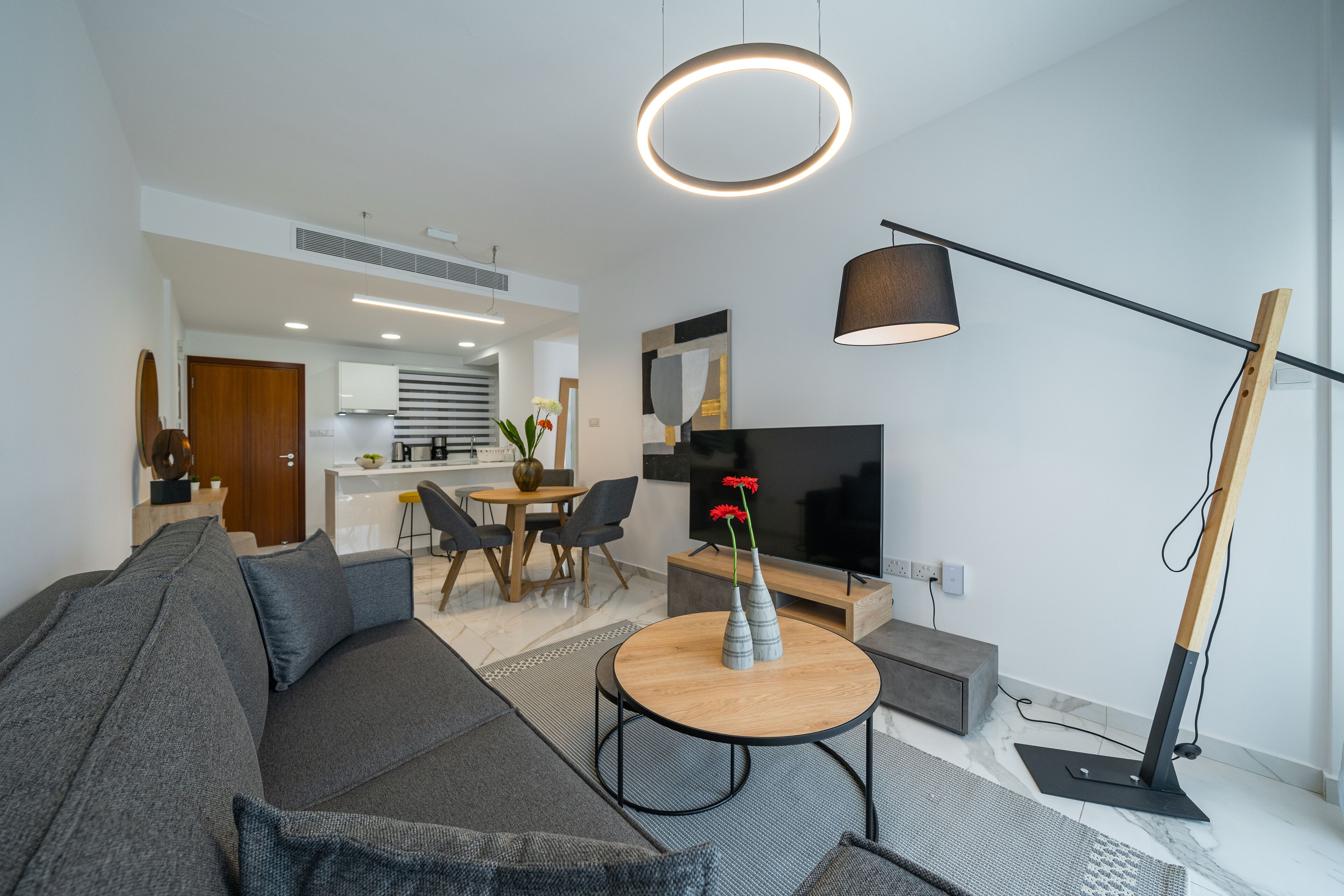 A modern living room with a sofa, a round coffee table, a TV, and a dining area in the background.