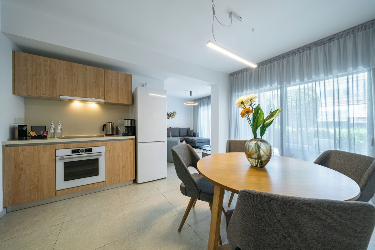 A modern kitchen with wooden cabinets, a built-in oven, and a dining area with a round table and chairs.