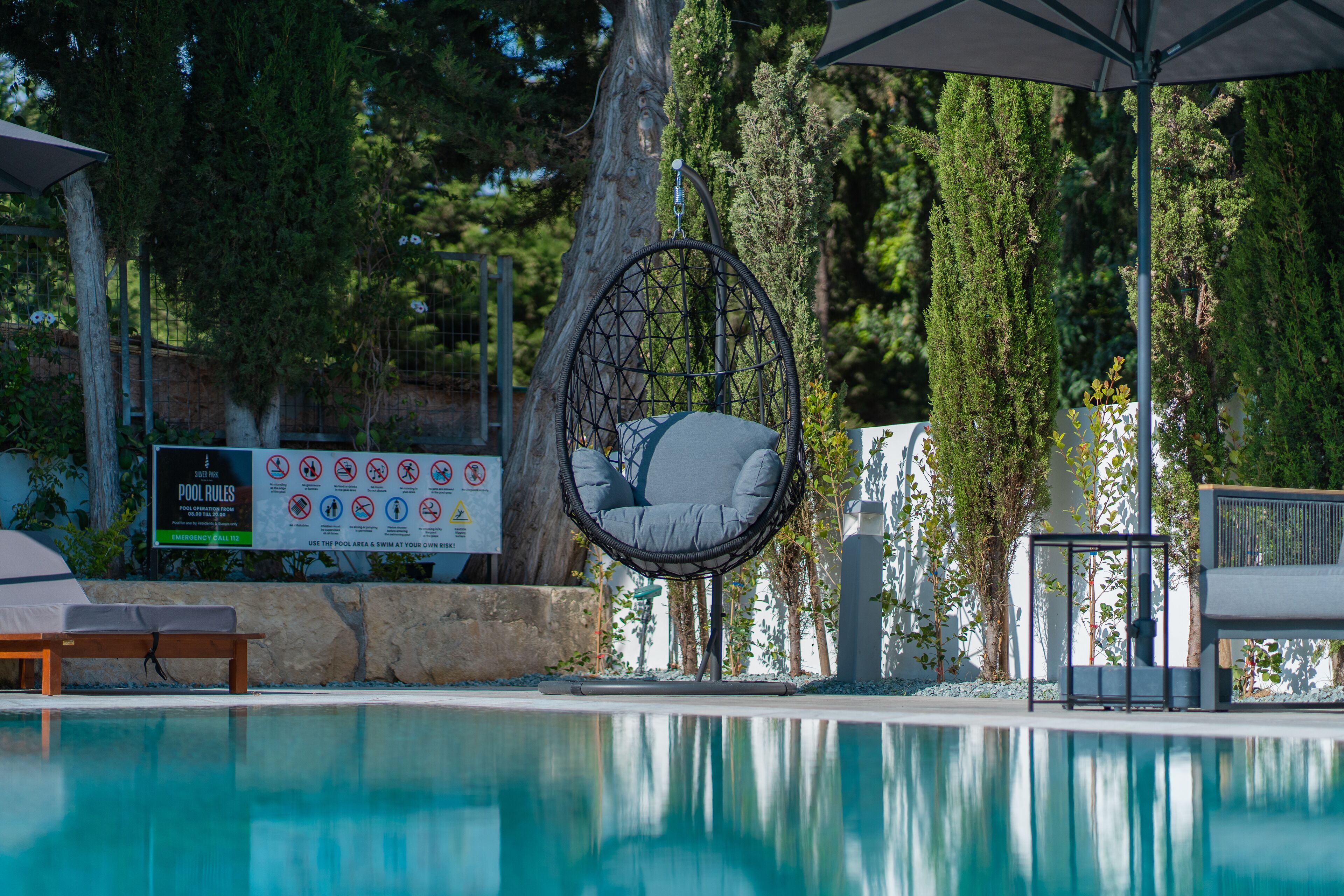 A pool area with a hanging chair, a lounge chair, and a sign with pool rules.