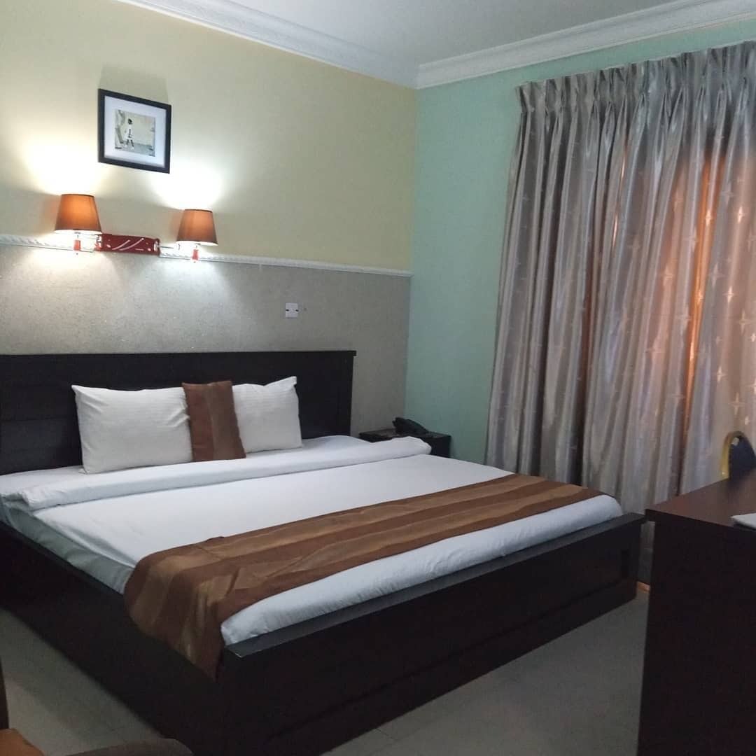 Habitación de hotel con cama, dos lámparas de noche, un cuadro en la pared y una cortina en la ventana.