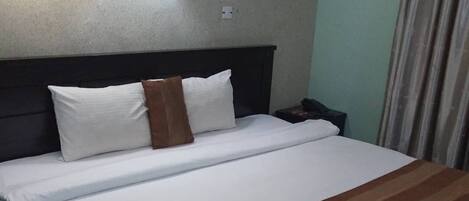 A neatly made bed with white and brown bedding, a dark headboard, and two wall-mounted lamps.