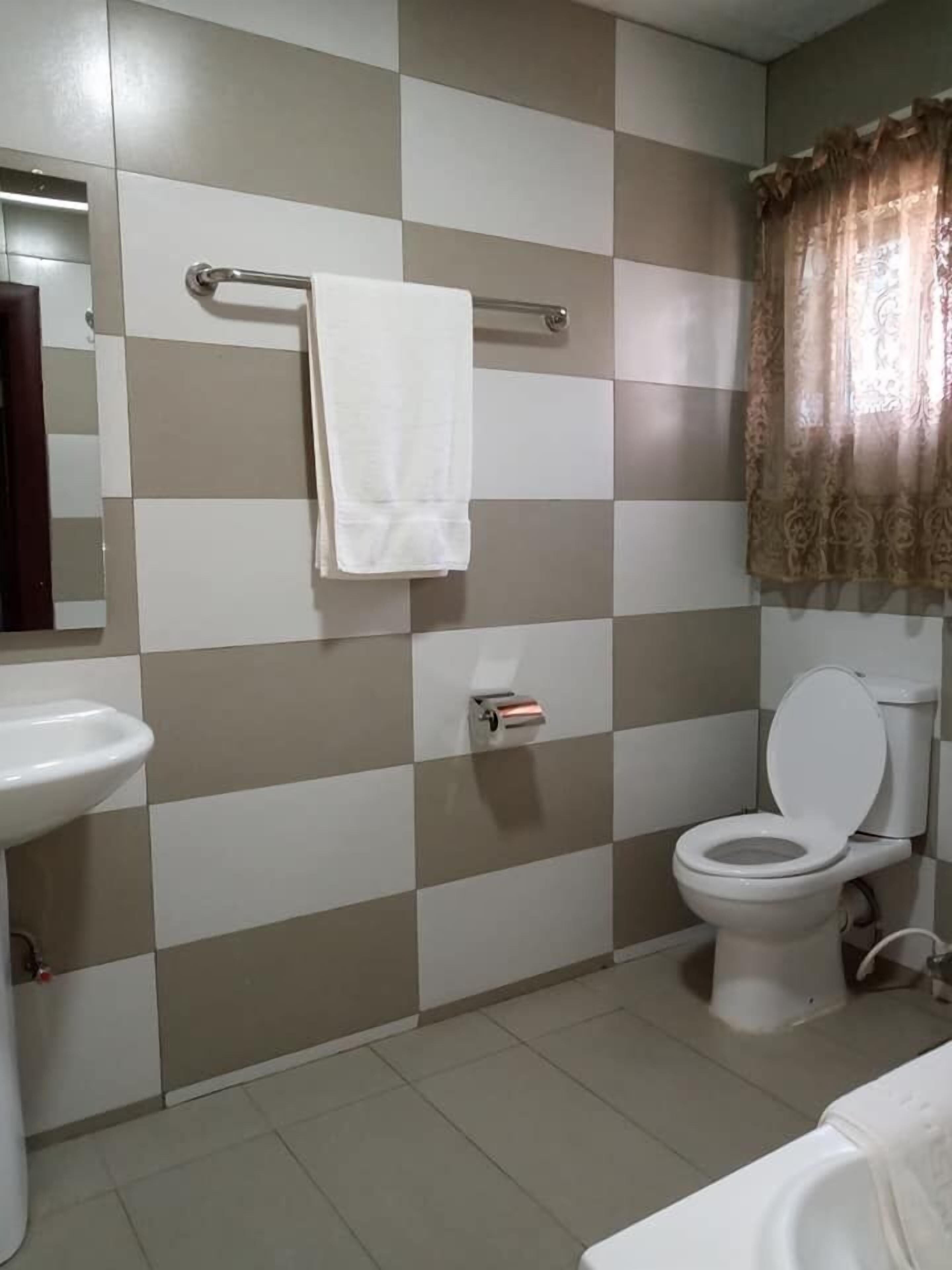 Een badkamer met een betegelde muur in ruitpatroon, een toilet, een wastafel en een handdoekhouder.