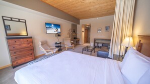 Une chambre d’hôtel avec un grand lit, une commode en bois, un bureau avec une chaise, une petite table et une cheminée.