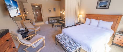 A hotel room with a large bed, a desk, a chair, a bench, and a TV mounted on the wall.