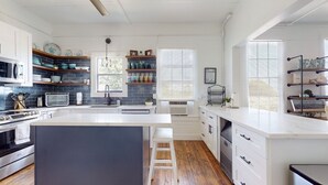 A modern kitchen with a central island, white cabinetry, and a blue-tiled backsplash. - 5 bedrooms, 2 1/2 bathrooms, sleeps 21 guests, and pet friendly. (Port Bolivar)