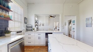 A modern kitchen with white cabinetry, a marble countertop, and a ceiling fan. - 5 bedrooms, 2 1/2 bathrooms, sleeps 21 guests, and pet friendly. (Port Bolivar)