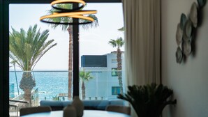 A dining area with a view of the sea and palm trees, a modern building with 'WellraSpa' signage, and a round table with chairs. - Waterside by Deserve (Paphos)