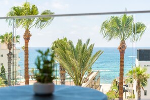 A balcony with a view of the sea, palm trees, and a building with the sign "ALMY". - Waterside by Deserve (Paphos)
