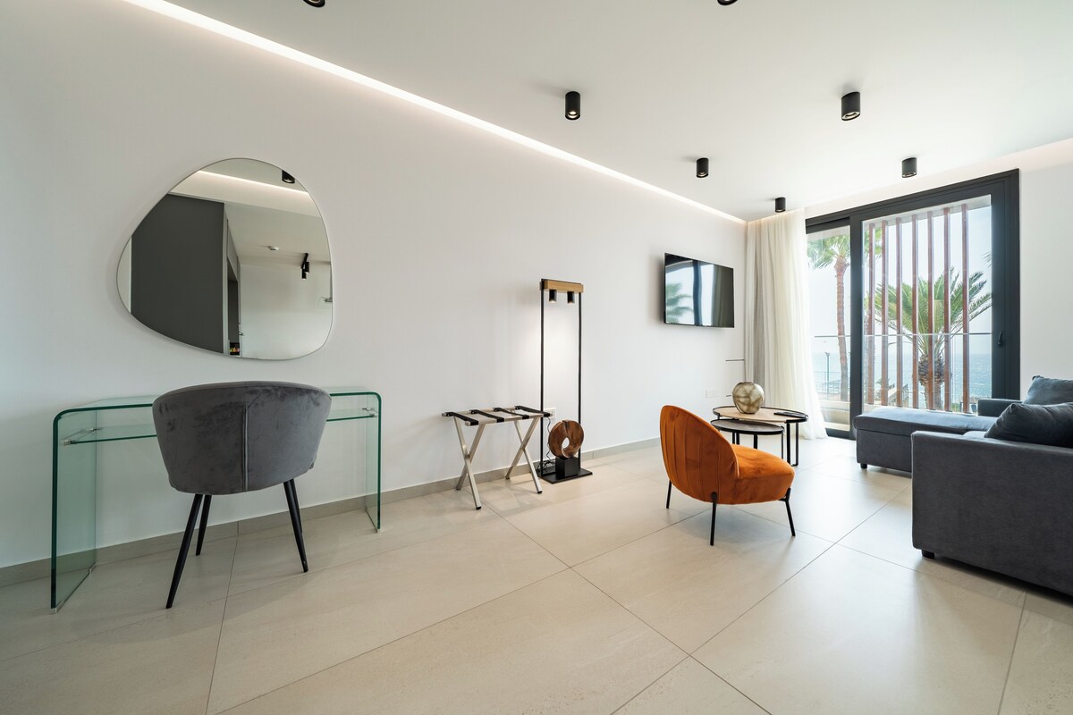A modern living room with a glass coffee table, a round mirror, a tall floor lamp, and a sofa.