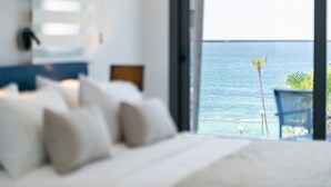 A bedroom with a large bed, a nightstand, and a view of the ocean through an open door. - Waterside by Deserve (Paphos)