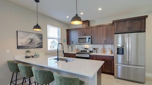 A modern kitchen with a central island, bar stools, stainless steel appliances, and dark wooden cabinets.