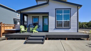 A modern house with a deck, two green chairs, and a blue door.