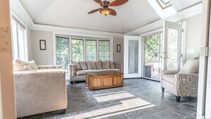 A spacious living room with a high ceiling, large windows, and a ceiling fan. - The Gemini House | Spacious Pinehurst Golf Retreat (Pinehurst)