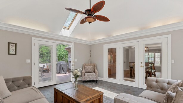 A spacious living room with a high ceiling fan, a large wooden coffee table, and a beige sofa. - The Gemini House | Spacious Pinehurst Golf Retreat (Pinehurst)