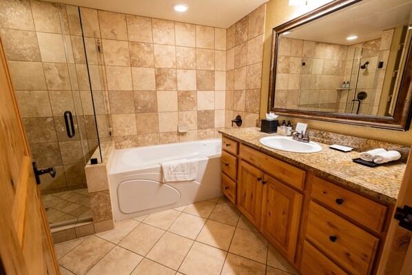 Un baño con bañera, lavamanos, armarios de madera, un espejo grande y zona de ducha.