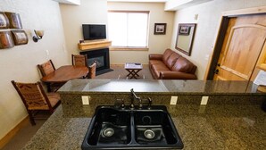 A kitchen with a double sink, a dining table with chairs, a fireplace, a television, and a sofa. - Silverado Lodge - 1 BR Suite, King Bed & Pool View by RedAwning (Park City)