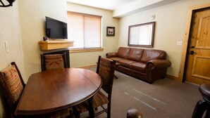 A living room with a wooden dining table, leather sofa, and a TV mounted on the wall. - Silverado Lodge - 1 BR Suite, King Bed & Pool View by RedAwning (Park City)
