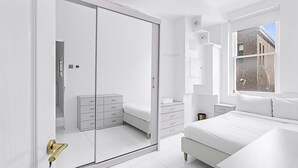 Ein modernes Schlafzimmer mit großem Kleiderschrank, Nachttisch, Bett und Fenster mit Blick auf ein Backsteingebäude.