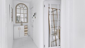 Ein Flur mit weißen Wänden, einer weißen Tür mit goldener Rahmung und einem weißen Schrank mit Schubladen.