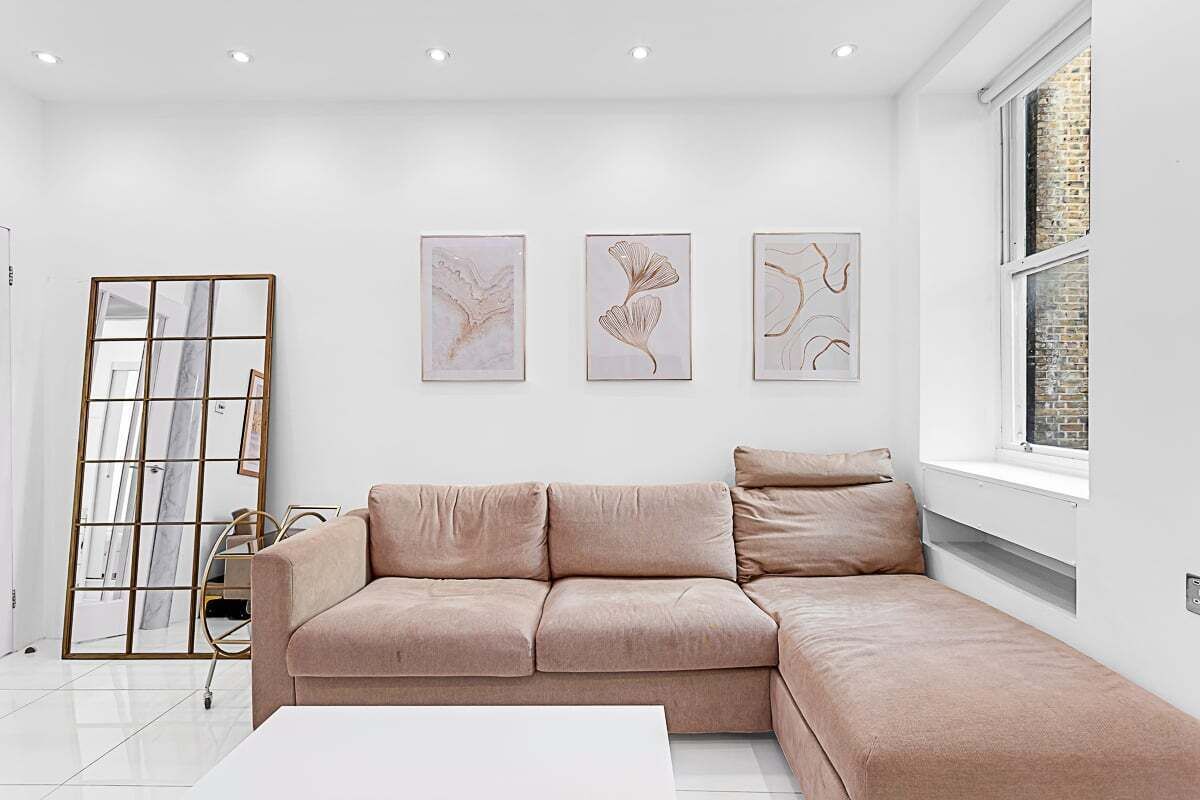 Un salon moderne avec un canapé d’angle beige, une table basse blanche et trois œuvres d’art abstraites encadrées accrochées au mur.