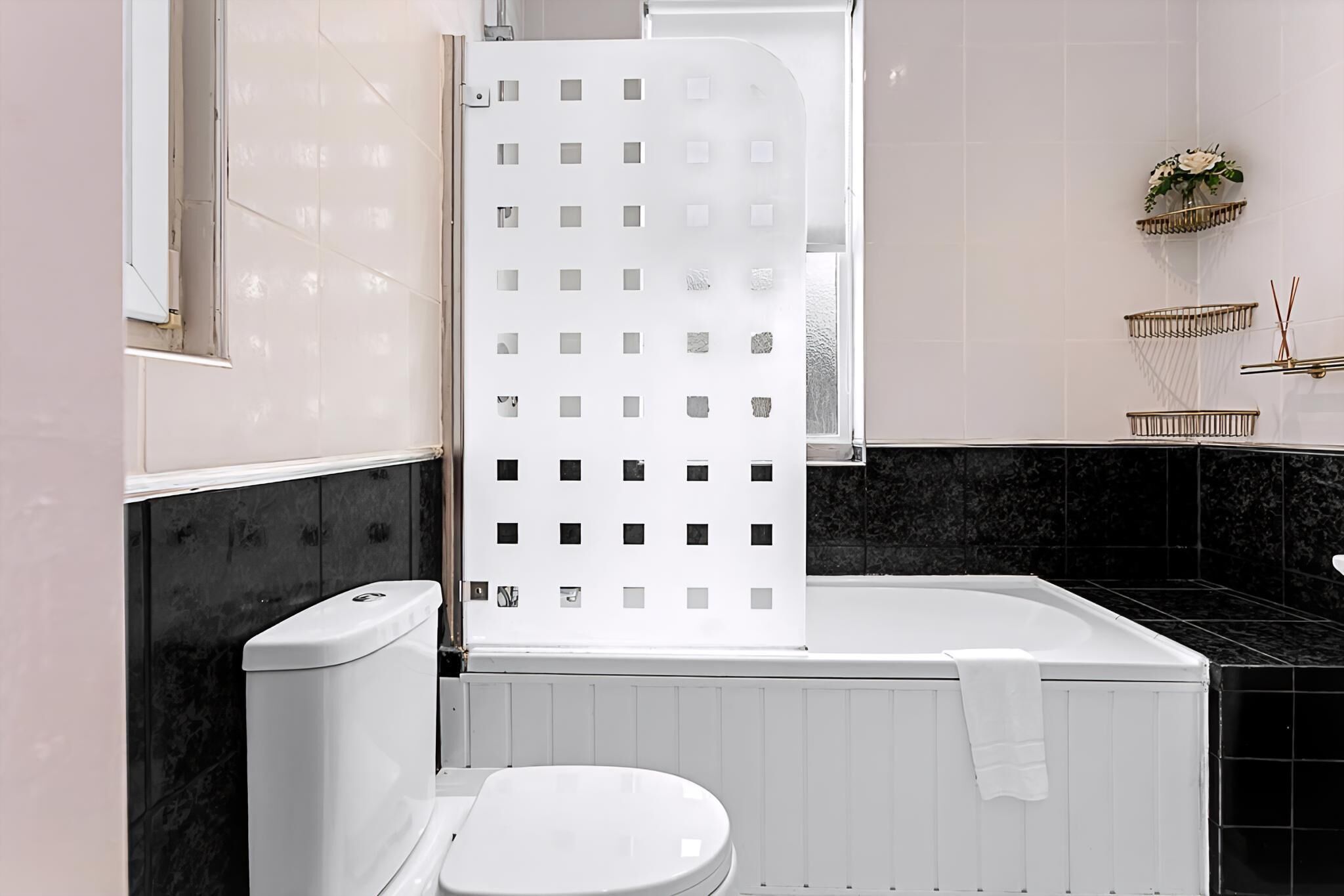 Un baño moderno con inodoro blanco, bañera blanca con toalla y cabina de ducha con puerta de vidrio esmerilado.