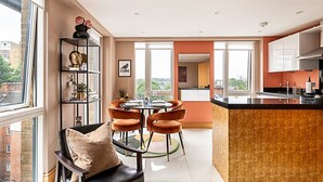 Eine moderne Küche mit einer zentralen Kochinsel, Essbereich mit orangefarbenen Stühlen und Blick auf die Stadt durch große Fenster.
