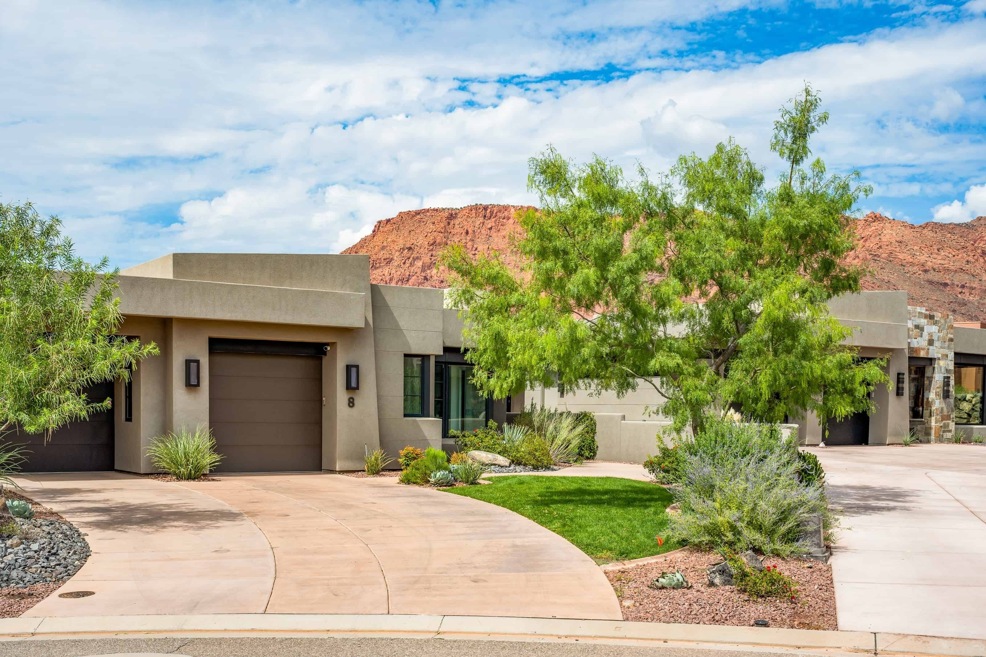A modern two-story house with a garage, surrounded by landscaped gardens and a mountain backdrop.