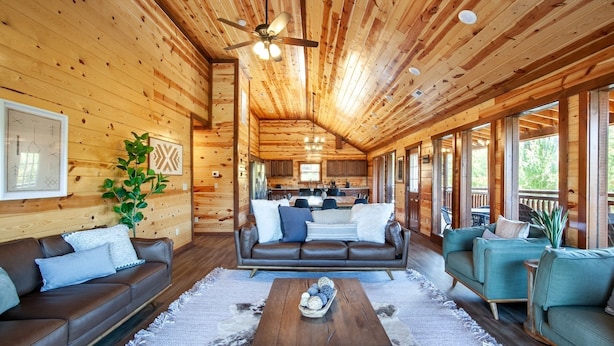 A spacious cabin interior with a central seating area, a kitchen, and large windows. - Splash Of Gatlinburg 6 Bedroom Cabin by RedAwning (Gatlinburg)