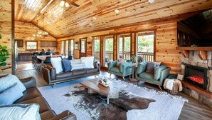 A spacious living area with a fireplace, leather sofas, and a dining area with a kitchen in the background. - Splash Of Gatlinburg 6 Bedroom Cabin by RedAwning (Gatlinburg)