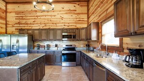 A spacious kitchen with wooden paneling, granite countertops, stainless steel appliances, and a central island. - Splash Of Gatlinburg 6 Bedroom Cabin by RedAwning (Gatlinburg)