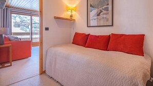 A bedroom with a bed, red pillows, a nightstand, a lamp, and a framed picture on the wall. - 5m from ski slopes, floor -5, view ski slopes, balcony, 25m², Méribel-Mottaret (Méribel - Les Allues)