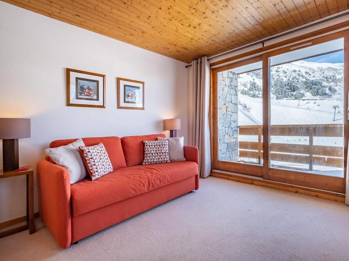 A cozy room with a red sofa, two framed pictures on the wall, and a large window offering a view of a snowy landscape.