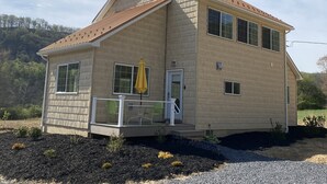 A two-story house with a sloped roof, a front porch with a railing, and a small garden area. - New build OWL HOUSE, quiet, near trails, stargazing! (Landisburg)