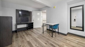 A modern, minimalist room with a wooden floor, a desk with a chair, a flat-screen TV, and a large mirror on the wall. - Southern Suites Carrollton (Carrollton)