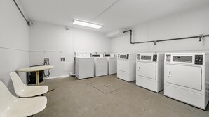 A laundry room with multiple washing machines, a table, and chairs. - Southern Suites Carrollton (Carrollton)