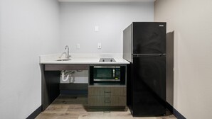 A compact kitchen with a built-in microwave, a sink, and a black refrigerator. - Southern Suites Carrollton (Carrollton)