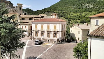 A street view with a building featuring a tiled roof, a bell tower, and a parking area.