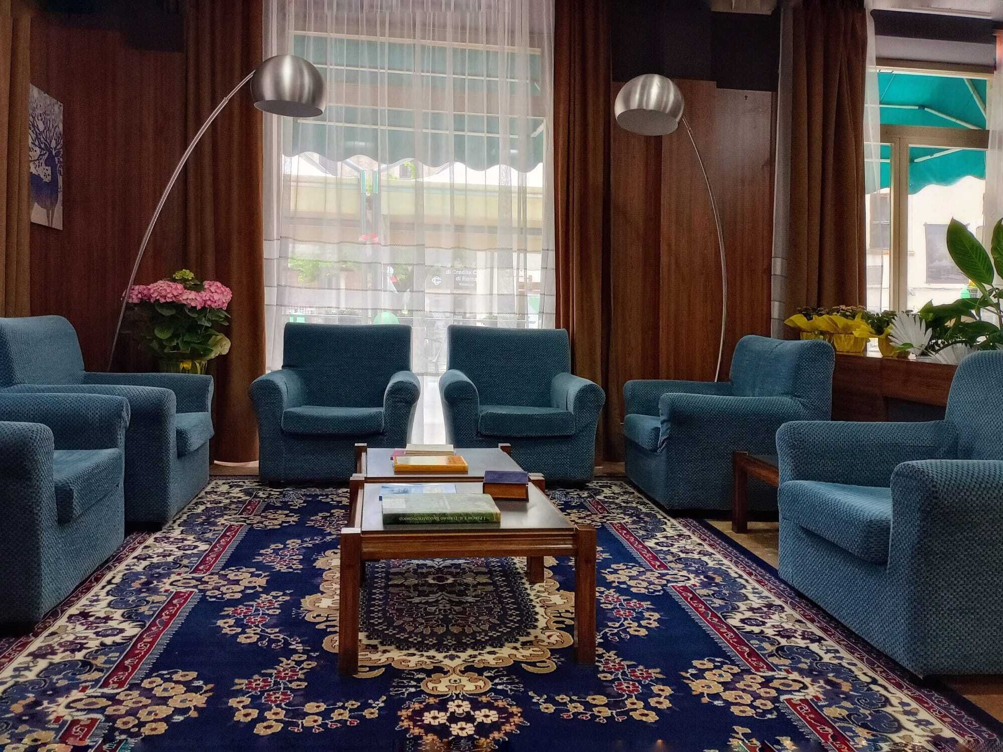 A room with four blue armchairs, a wooden coffee table with books, a patterned rug, and a large window with curtains.