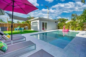 A backyard with a swimming pool, a pink flamingo float, and a patio area with a table and chairs. - Flamingo Retreat Steps to Downtown Pool home (Delray Beach)