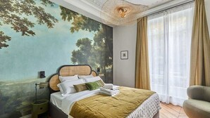 Ein Schlafzimmer mit einer großen Baum-Mural, einem Bett mit grüner Decke, einem Nachttisch und einer Hängelampe.
