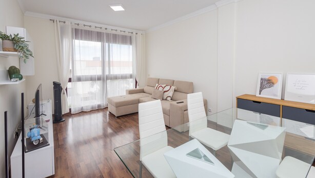 A modern living room with a glass dining table, a beige sofa, and a large window with sheer curtains. - Luxury Workfriendly Home - Far Ocean Views (Santa Lucía de Tirajana)
