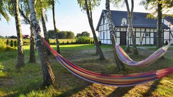A hammock in a grassy area with trees and a building in the background.