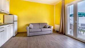 A compact living space with a kitchenette, a grey sofa, and a sliding glass door leading to an outdoor area. - Agriturismo Cascina Trevo (Spotorno)