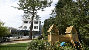 Een groot huis met een overdekte veranda en een houten speeltuintje.