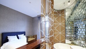 Een moderne hotelkamer met een groot bed, een houten nachtkastje, een grote spiegel en een badkamer met een ligbad en een douchecabine met glazen wanden.